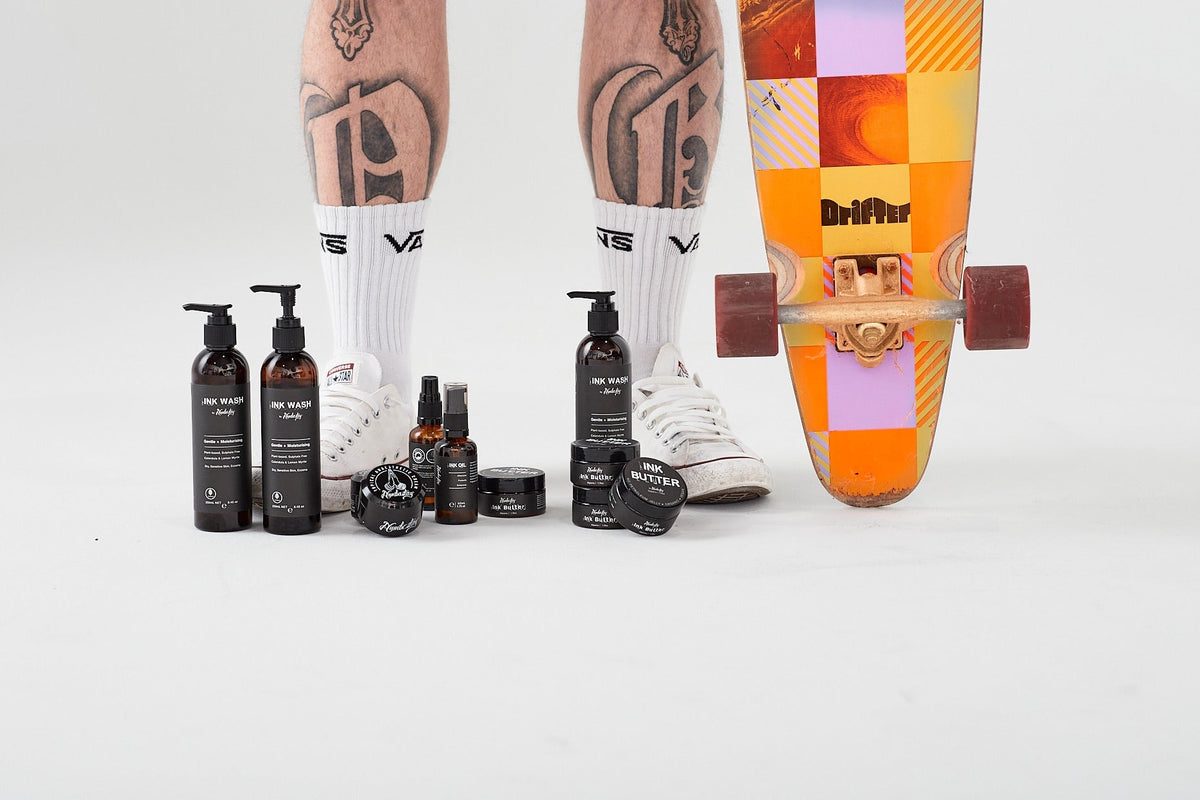 Numbastay products arranged beside a tattooed person’s legs and skateboard