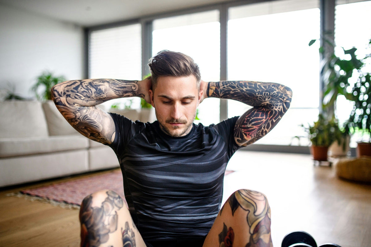 Tattooed man sitting with his hands behind his head in a bright room